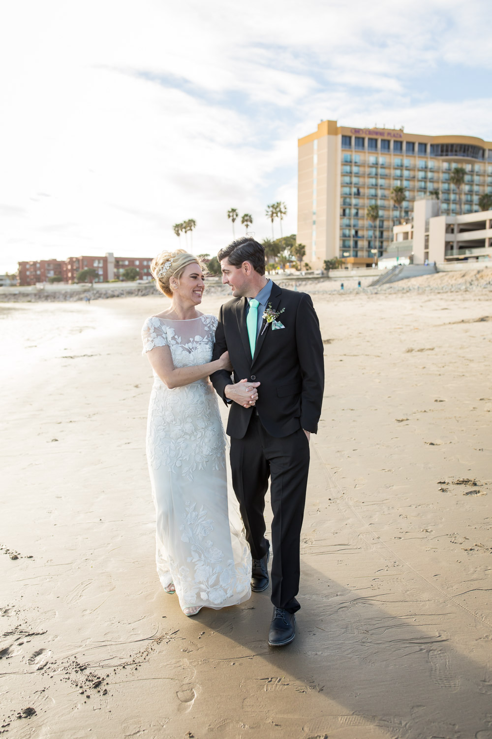 bride and groom walking on the beach in front of crowne plaza ventura