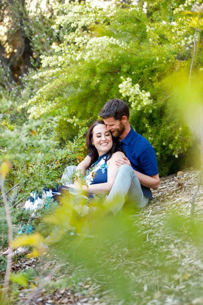 couple sitting around greenery at their engagement session