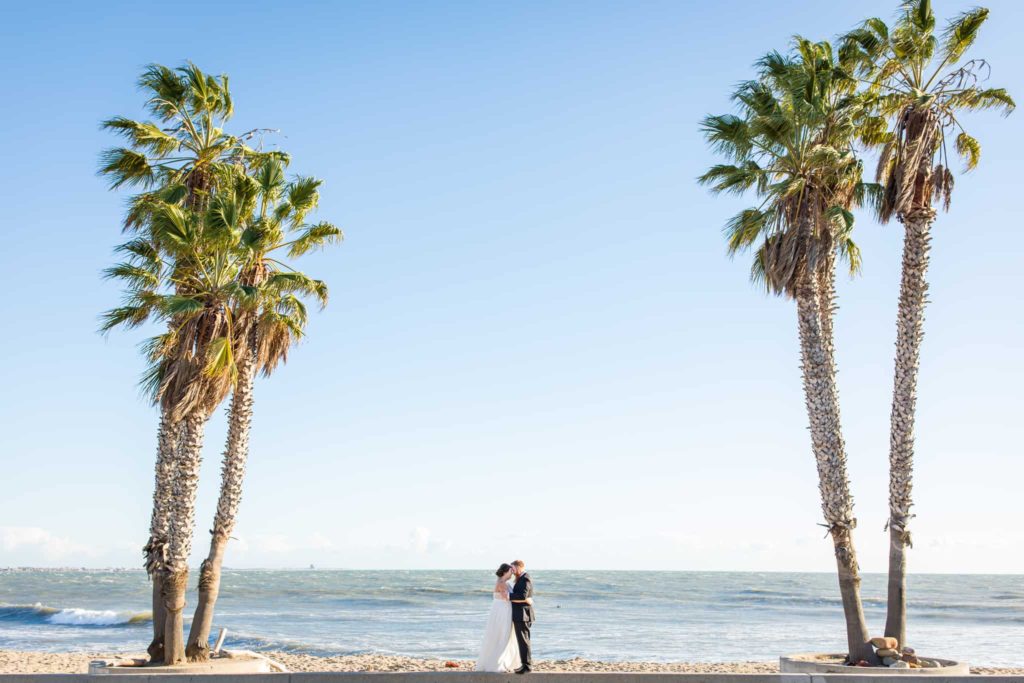 bride and groom by palm trees at the beach in ventura