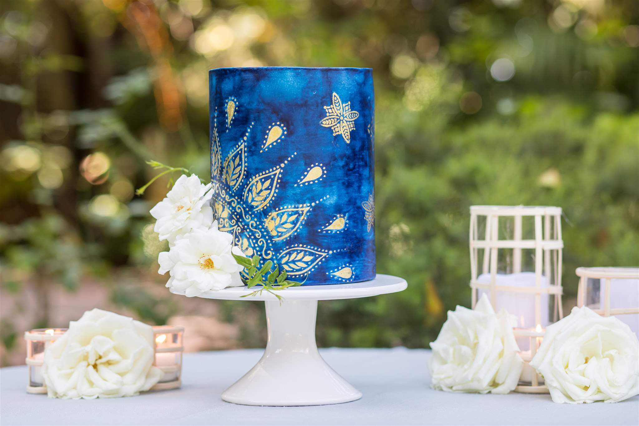 wedding cake table with dark blue cake on a white stand, lanterns and white florals at Hartley Botanica wedding venue