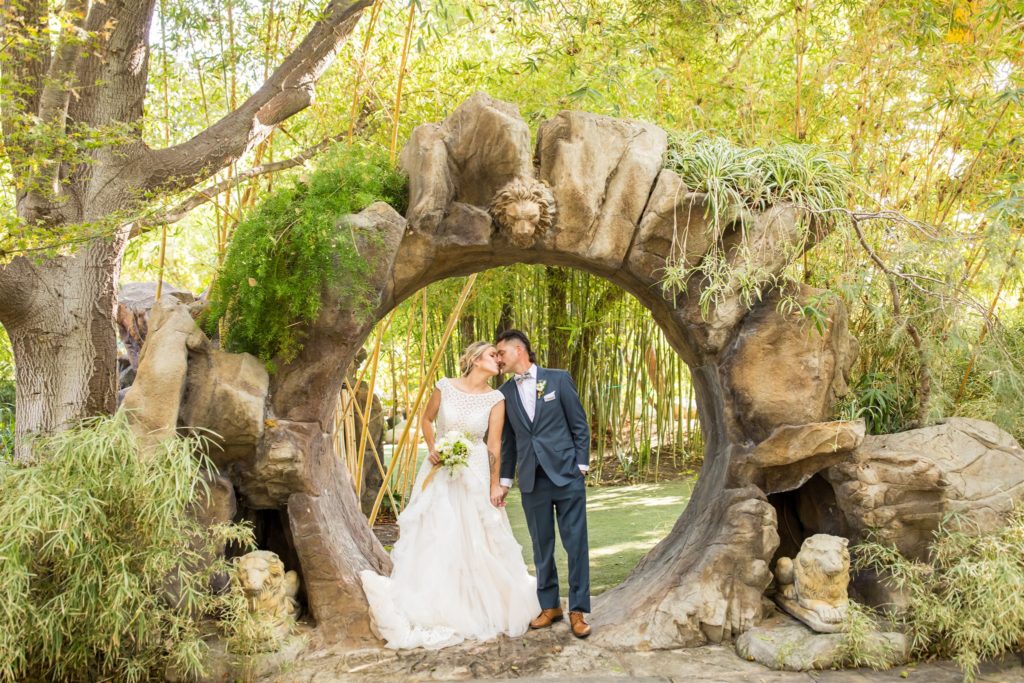 Somis California outdoor wedding venue with bride and groom holding hands and kissing each other under a stone arch at Hartley Botanica