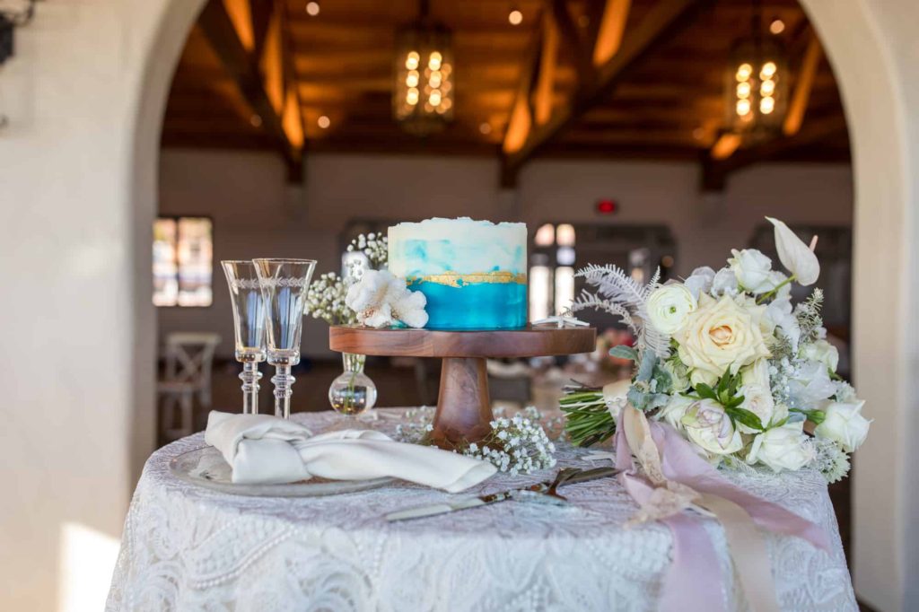 indoor wedding reception cake table with a blue back with gold detailing sitting next to a white floral bouquet