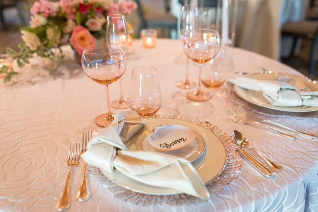 detail shot of table setting with a shell that reads "groom" on top of gold and white dishes