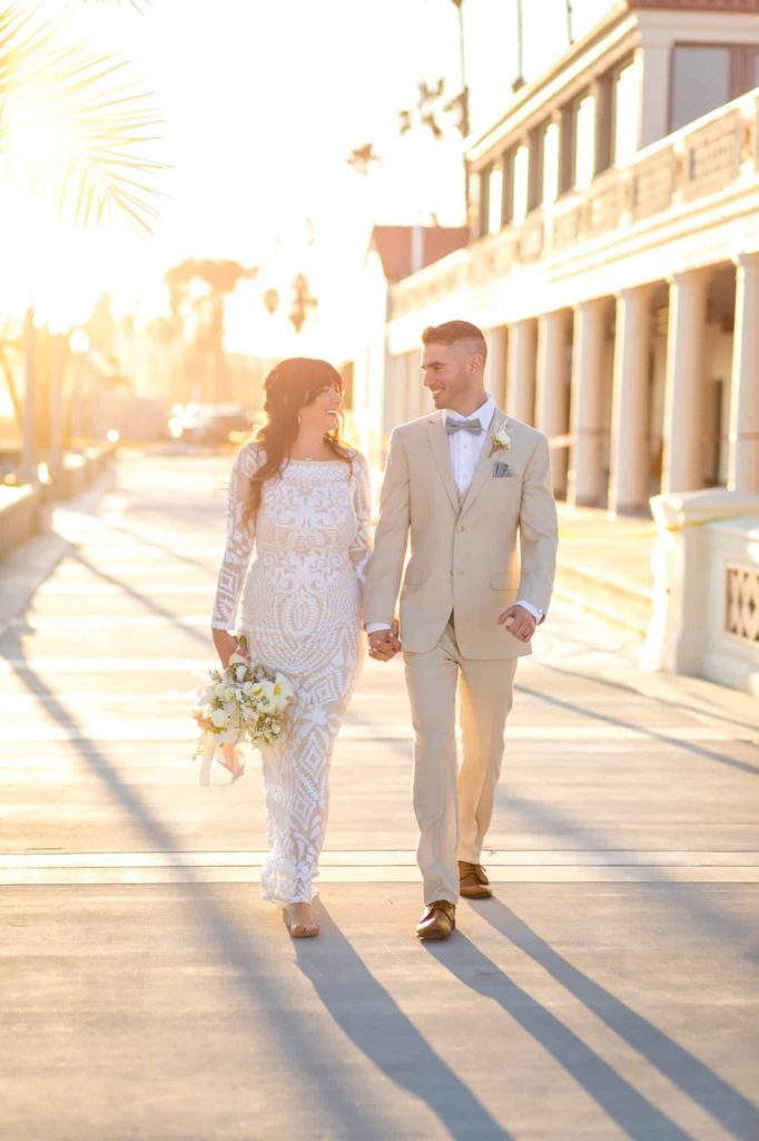 bride and groom holding hands and walking towards the camera as the sunsets behind them