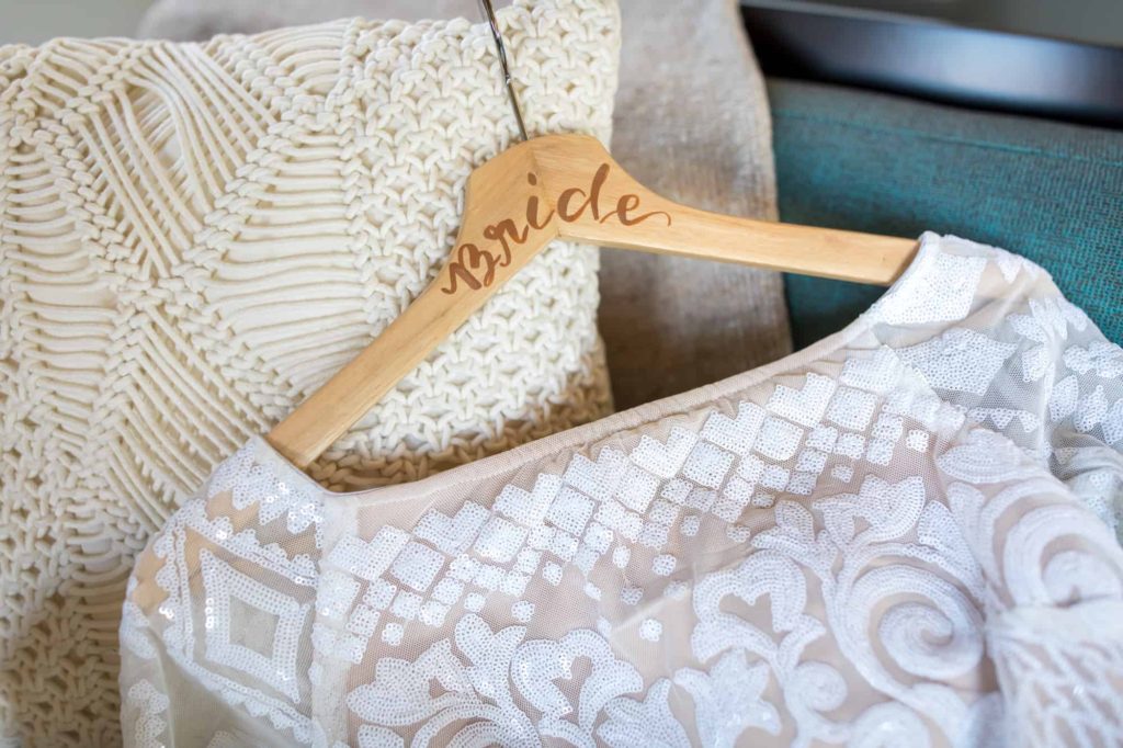 wood hanger with "bride" engraved on it holding a lace wedding dress