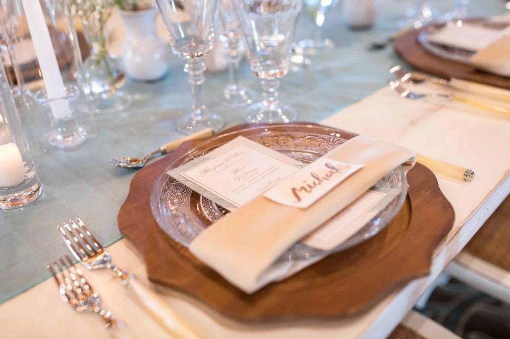 reception table setting with a wood plate topped with crystal dishes, a menu, napkin and custom calligraphy name tag