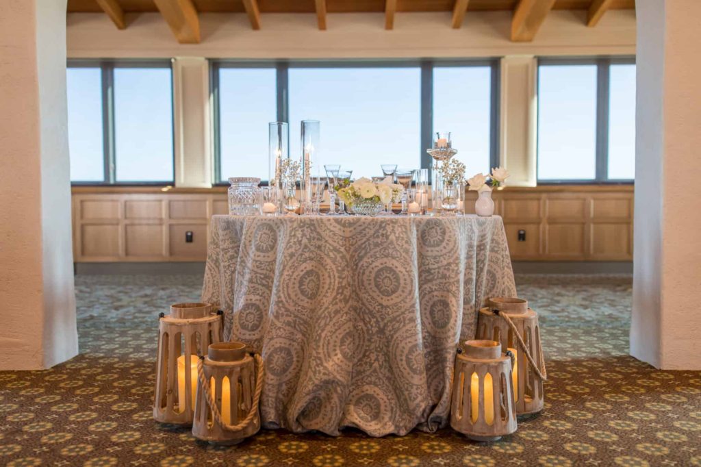 bride and groom table with a bohemian white and blue table cloth and wood lanterns for indoor reception at Cabrillo Pavilion wedding venue