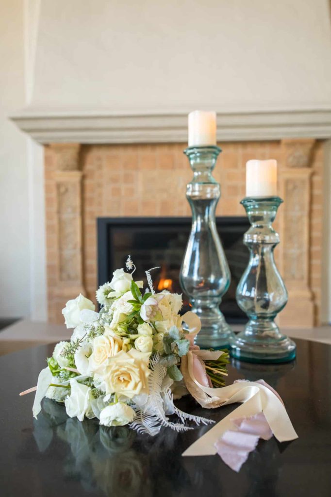 bridal bouquet filled with white roses and other florals sitting on a table with candle sticks