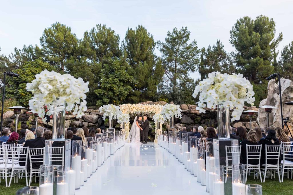 outdoor wedding ceremony space with all white decorations and tall trees as the backdrop