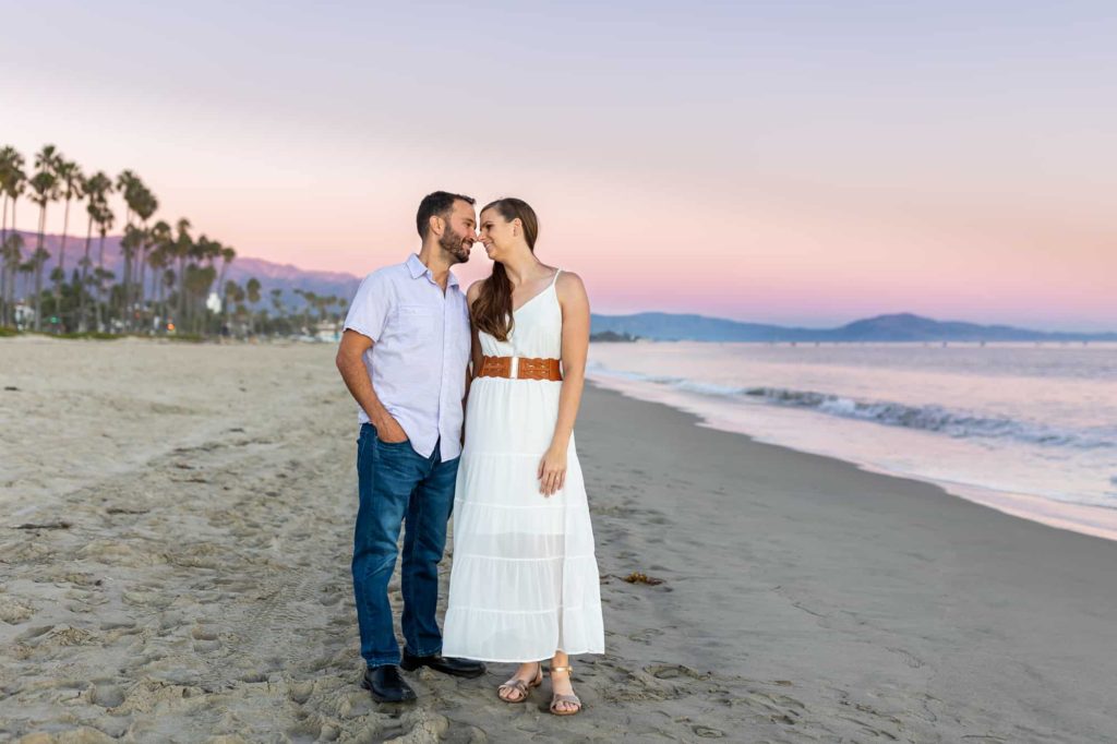 pink sunset engagement photos on the beach in Santa Barbara with man and woman looking at one another with their foreheads and noses touching, captured by best Santa Barbara wedding photographer