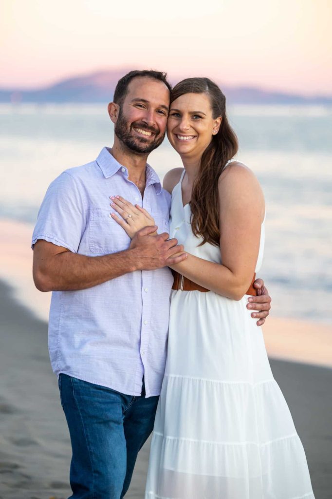beach engagement pictures in Santa Barbara with man in a blue shirt and woman in a white long dress posing together