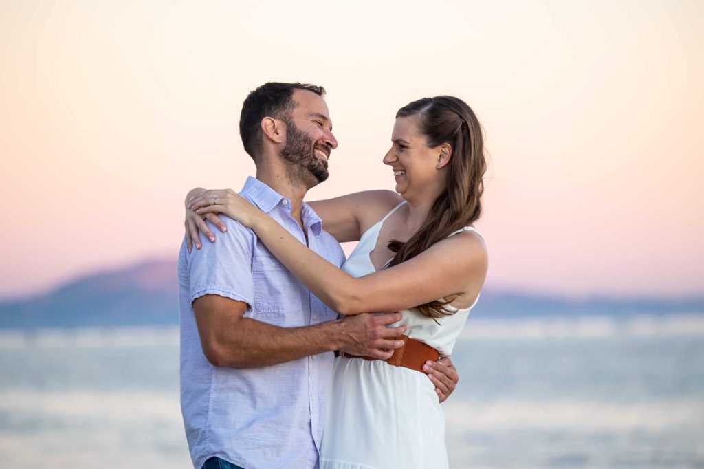 man and woman hugging each other on the beach and laughing for their Santa Barbara beach engagement photos