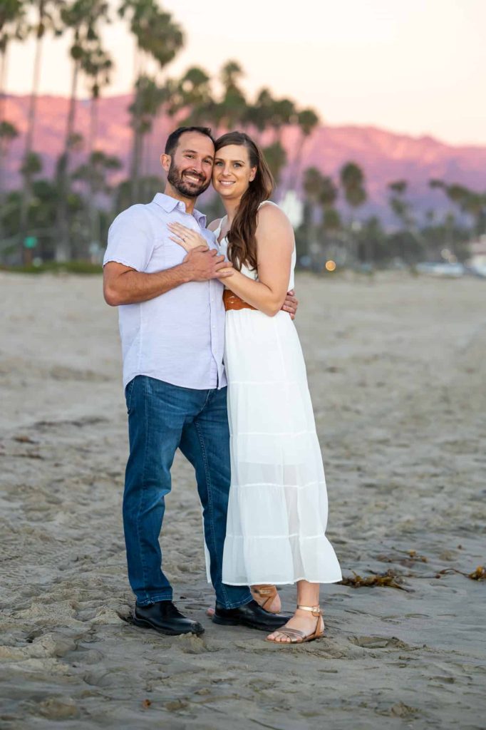 sunset beach engagement photos with man and woman in a white dress embracing each other for their summer engagement pictures