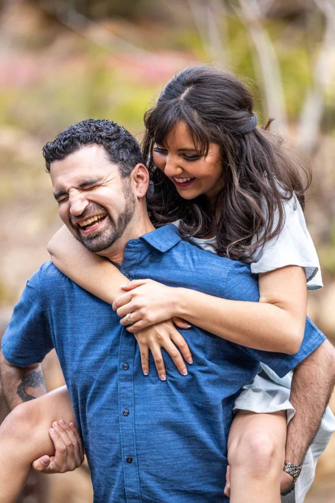 woman on a mans backs holding his shoulders as they laugh together during their Santa Barbara engagement photos