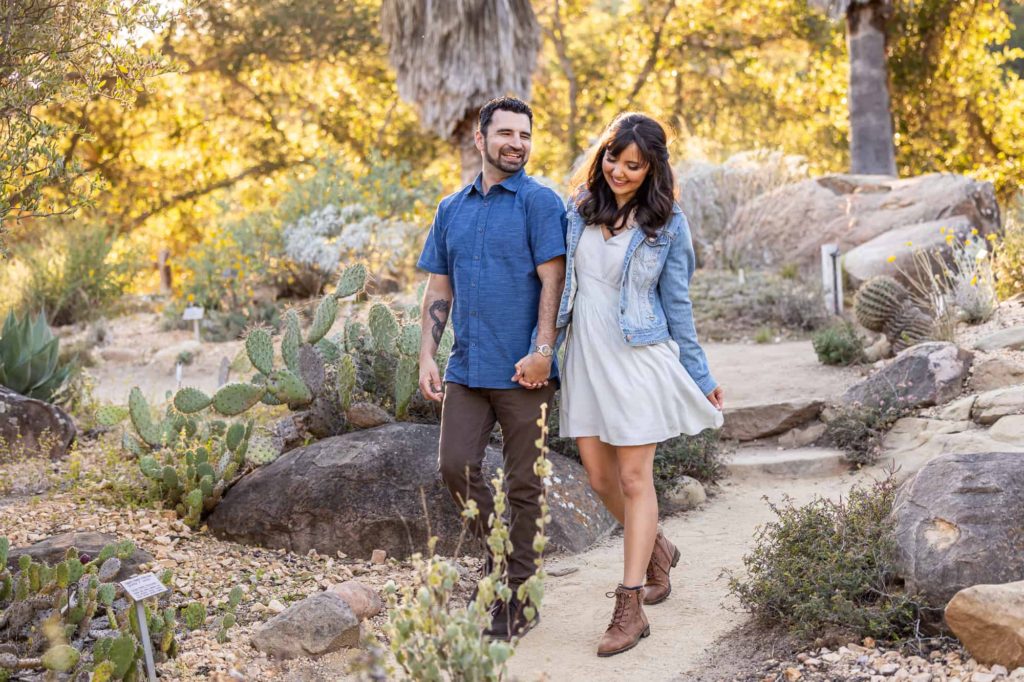 desert engagement session in Santa Barbara with man and woman holding hands and laughing as they walk through a trail