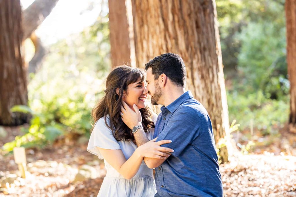 man caressing woman's cheek as they smile while sitting in the woods