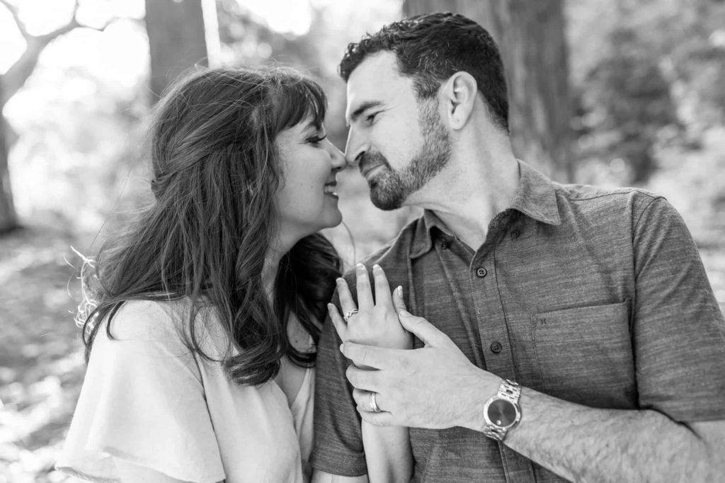 black and white engagement portrait with man and woman holding hands and touching their noses together and smiling