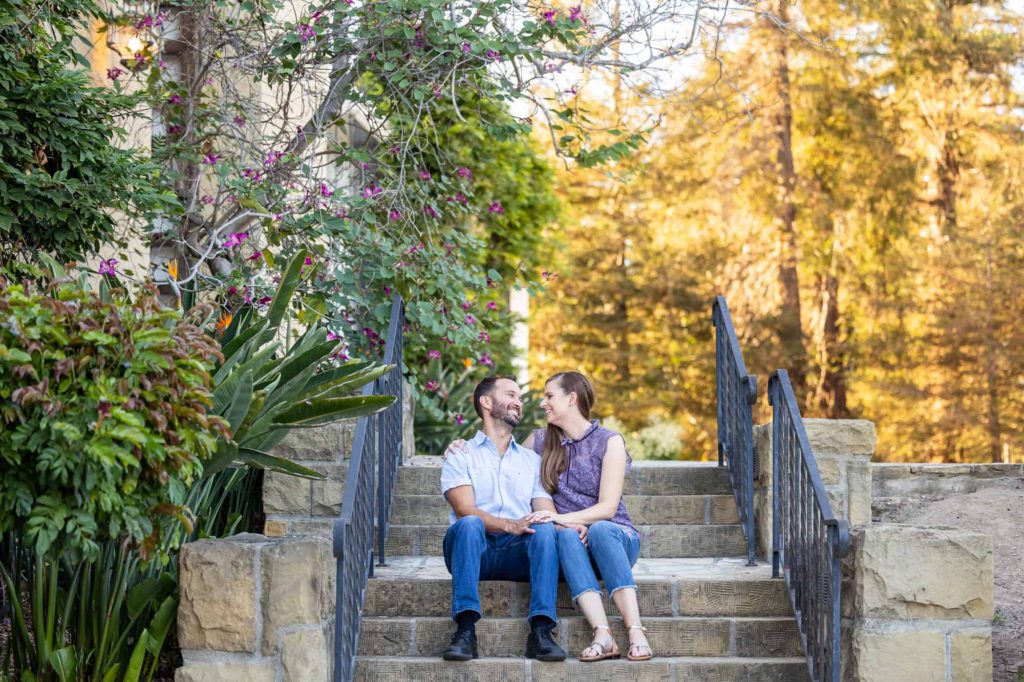 summer engagement photos with man and woman sitting on the stairs of a garden together captured by Santa Barbara wedding photographer