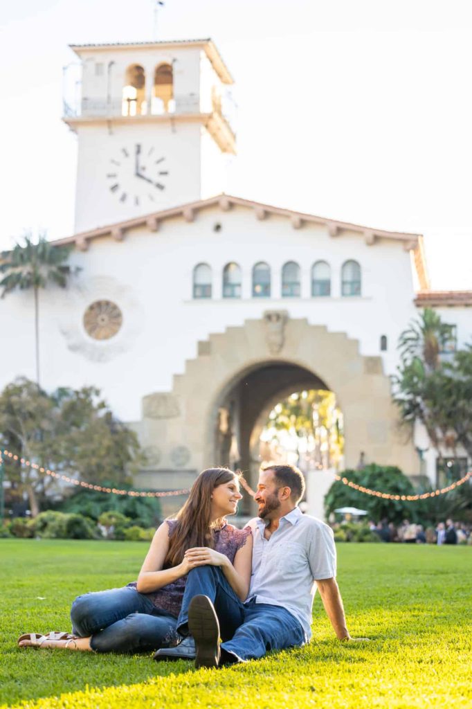 sun setting over the lawn of the Santa Barbara courthouse with couple sitting together on the lawn as they smile at each other