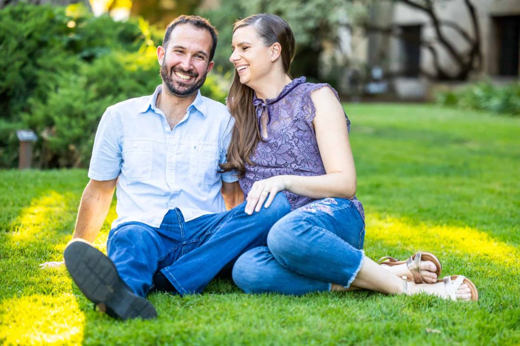 fiances sitting on the grass for their summer engagement pictures as they smile and laugh together, captured by best Santa Barbara wedding photographer