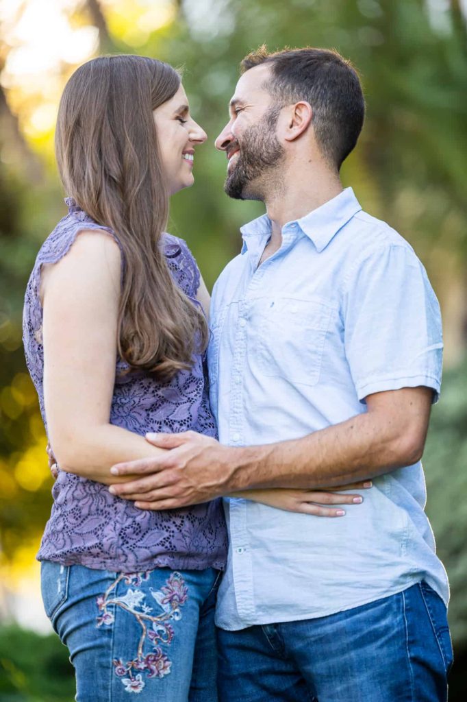 man and woman holding each other at the waist as they smile at each other in a garden for couples photos
