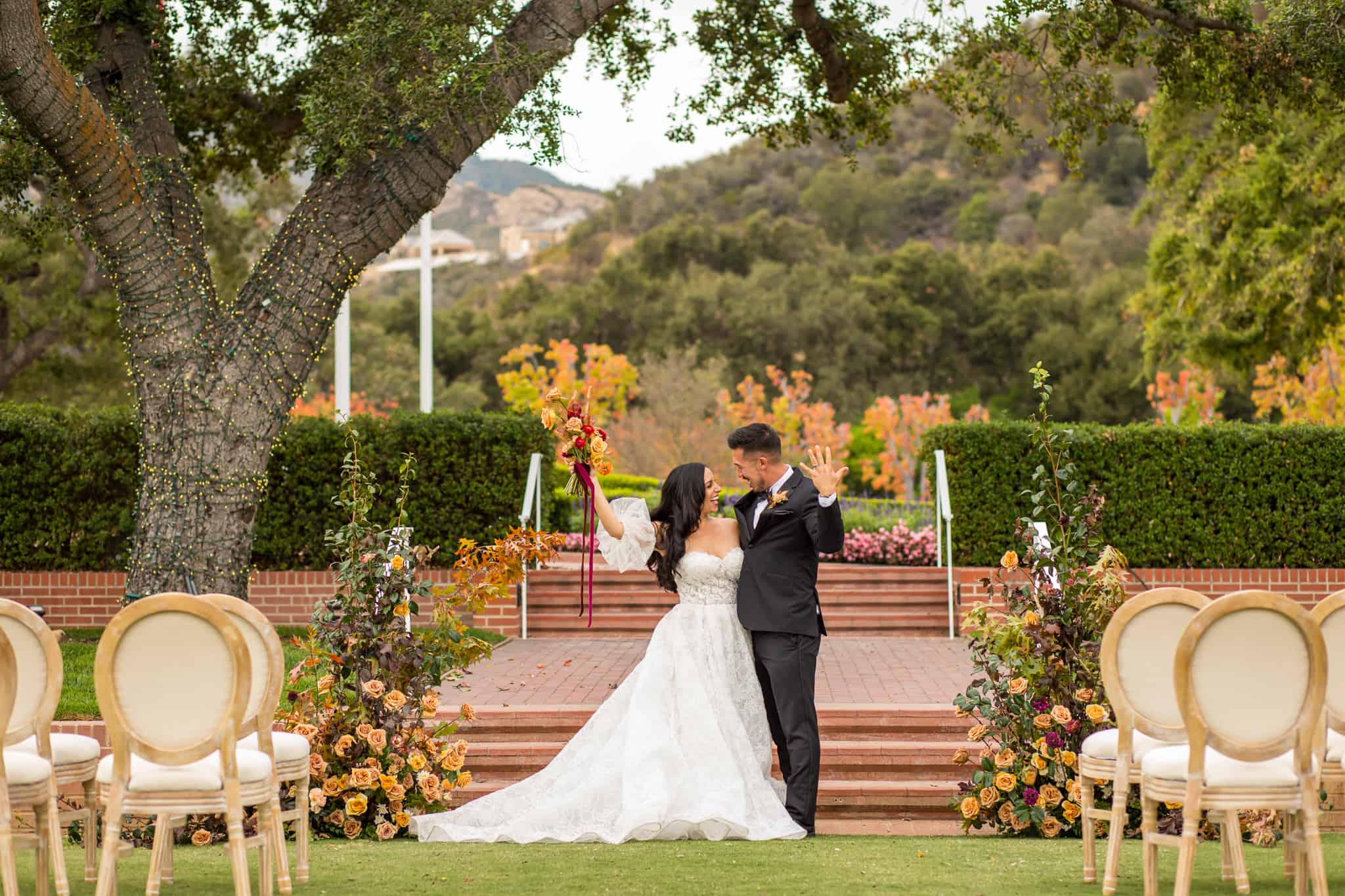 outdoor fall cermeony at Sherwood Country club with bride and groom hugging each other with one arm and raising their other arm in the air in celebration