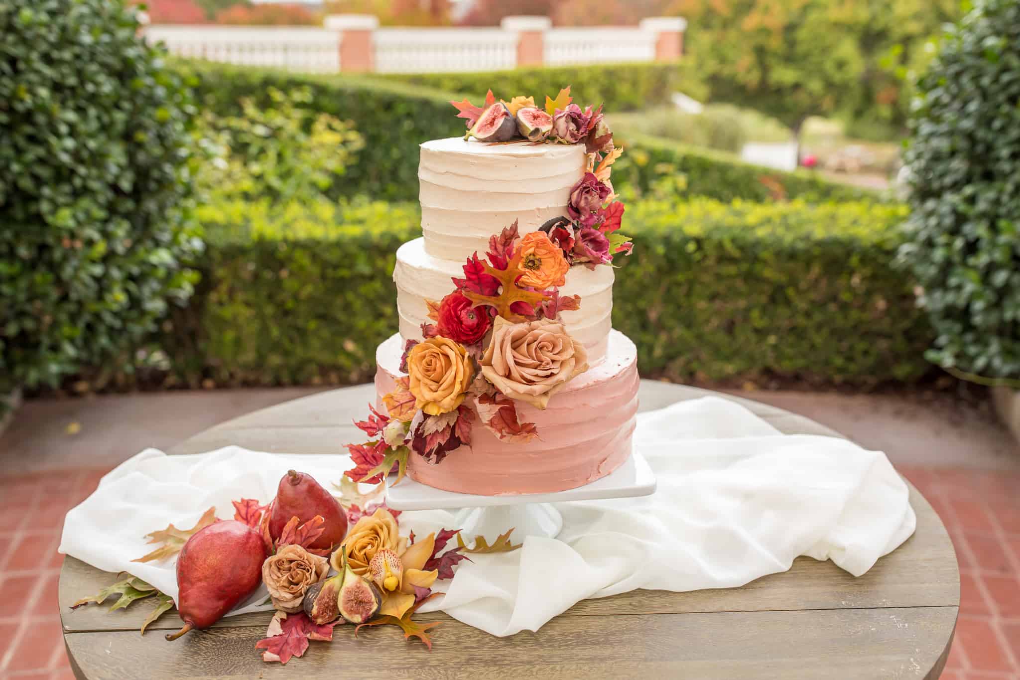 pink and cream wedding cake with fall leave and large roses wrapping around the three tears of the cake