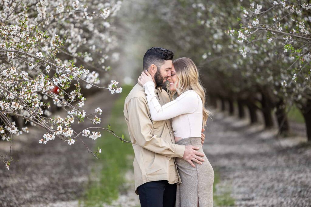 man and woman hugging each other and smiling with blossoms surrounding them, captured by best Central Valley California wedding photographer