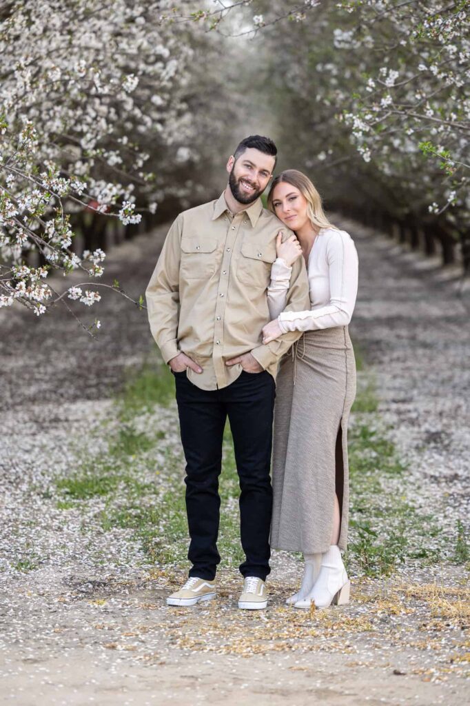 Central Valley California wedding photographer capture spring engagement session with woman embracing mans arm as they smile at the camera