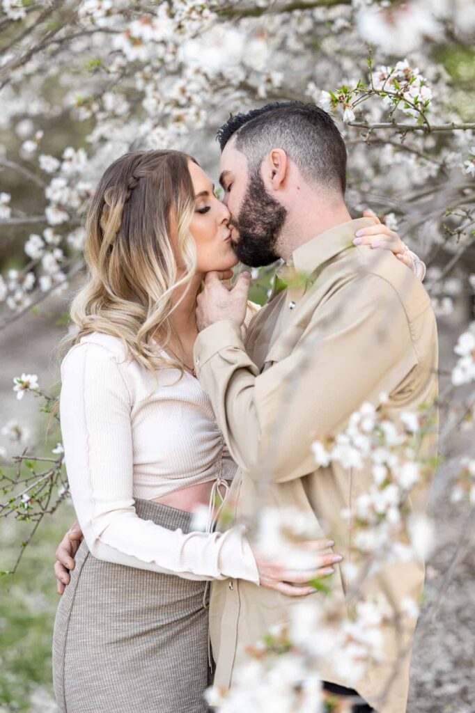 man and woman kissing in the blossoms of Central Valley almond orchard captured by best Central Valley California wedding photographer
