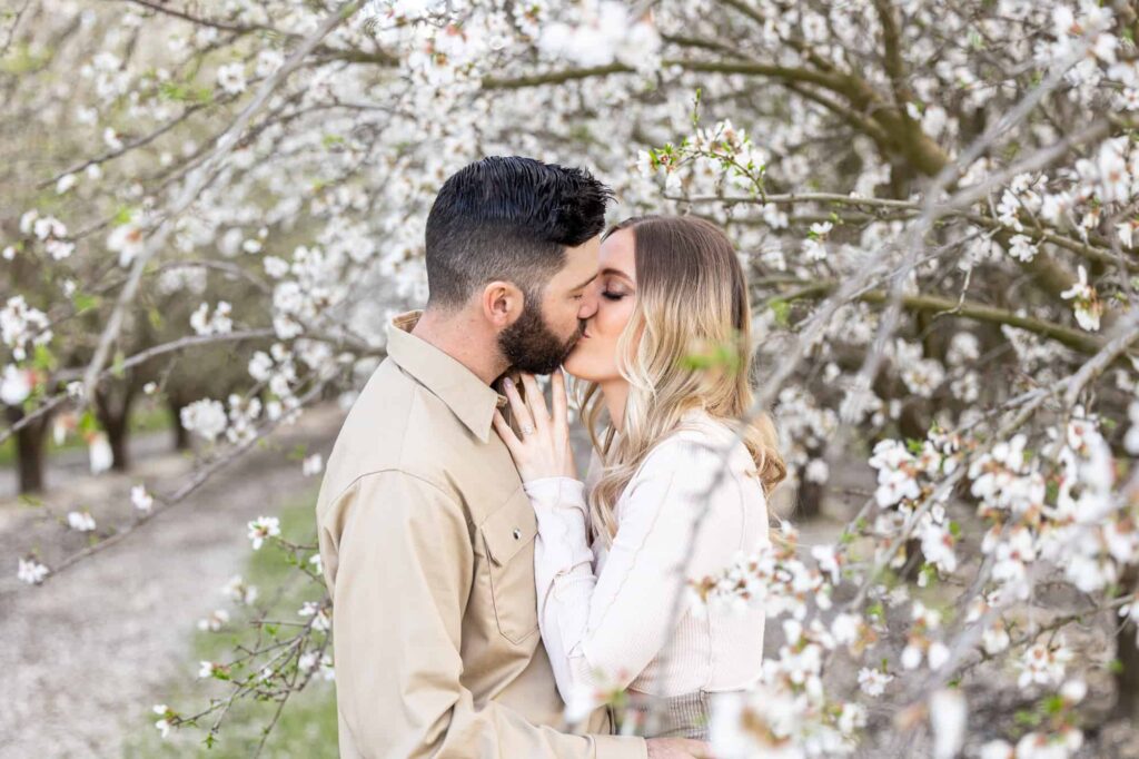 engaged couple kissing in the blossoms of an orchard