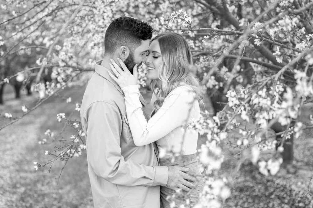 woman holding mans cheek and smiling as he holds her at her waist for their spring engagement photos
