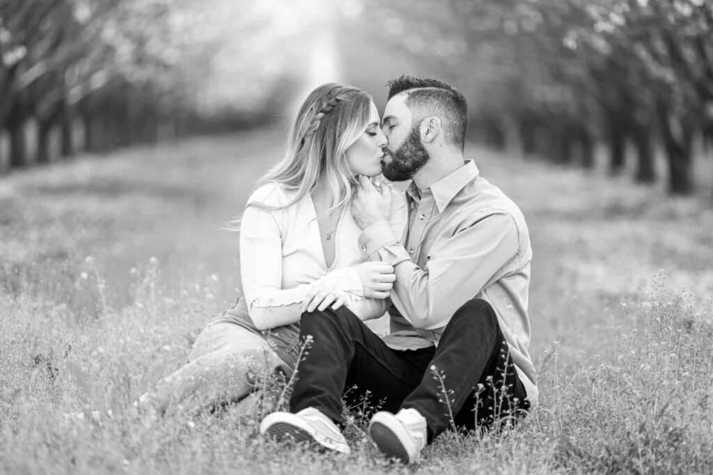 man and woman sitting together on the ground as the man caresses the woman's chin and kiss, captured by Central Valley California wedding photographer