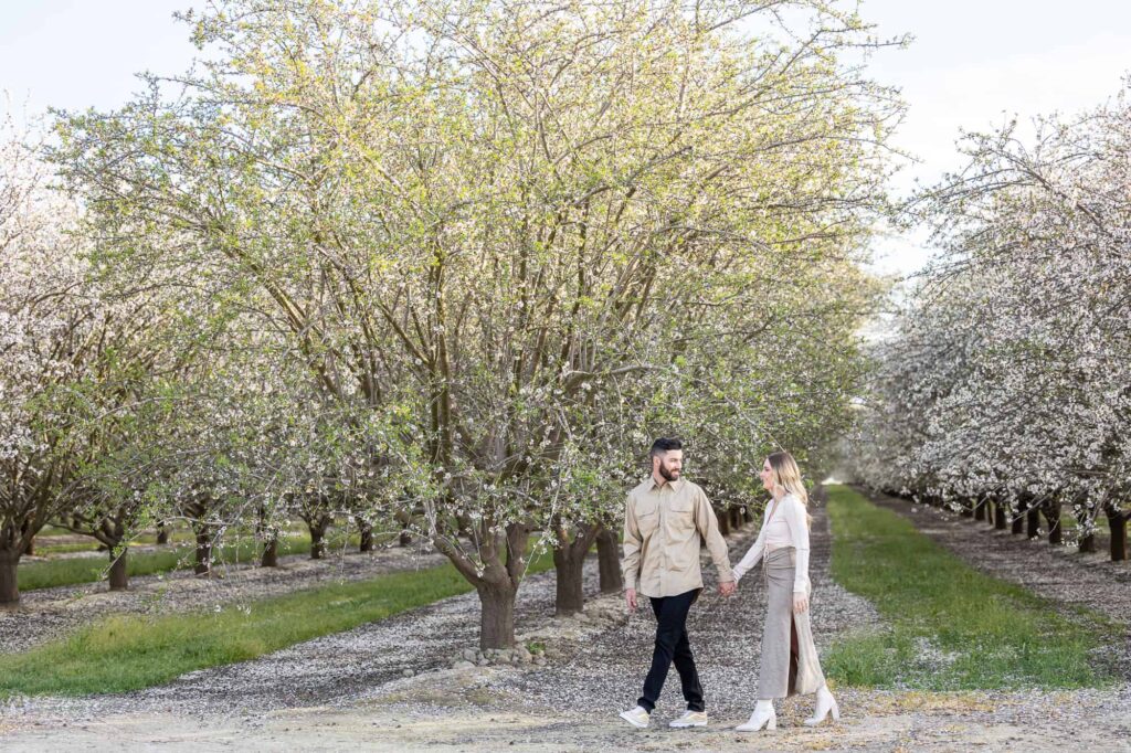 man holding womans hand and leading her through an almond orchard