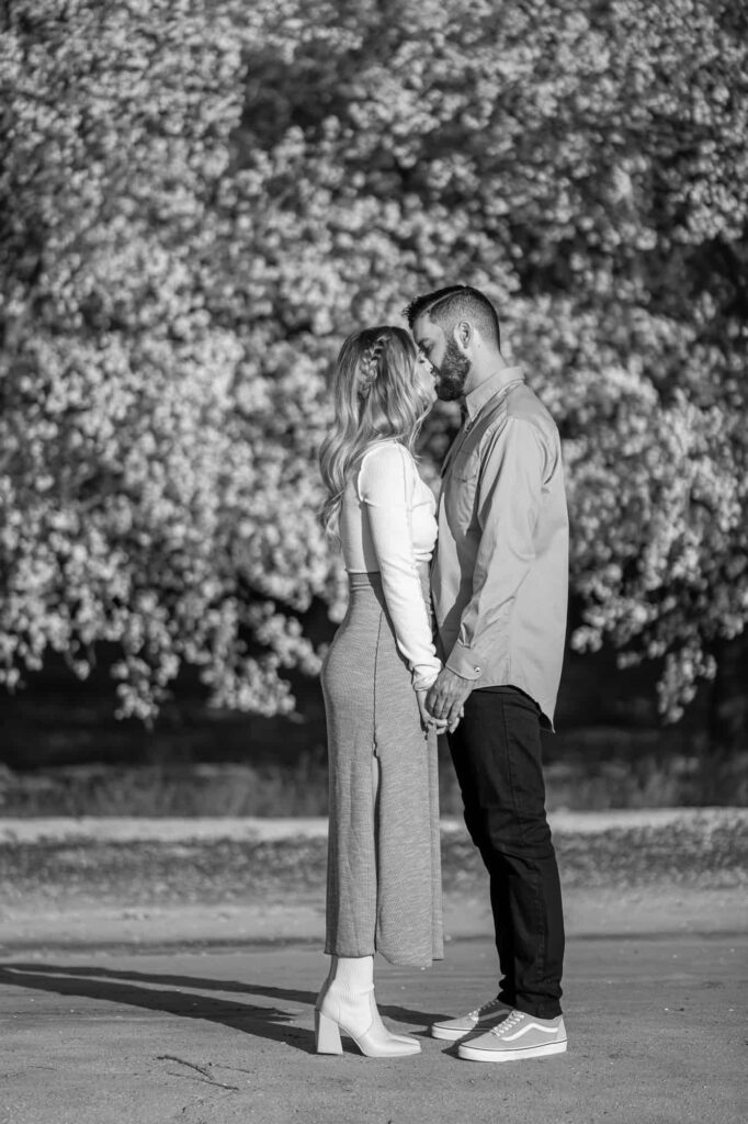 black and white engagement photo with woman and man holding hands and leaning into each other as they kiss, captured by Central Valley California wedding photographer