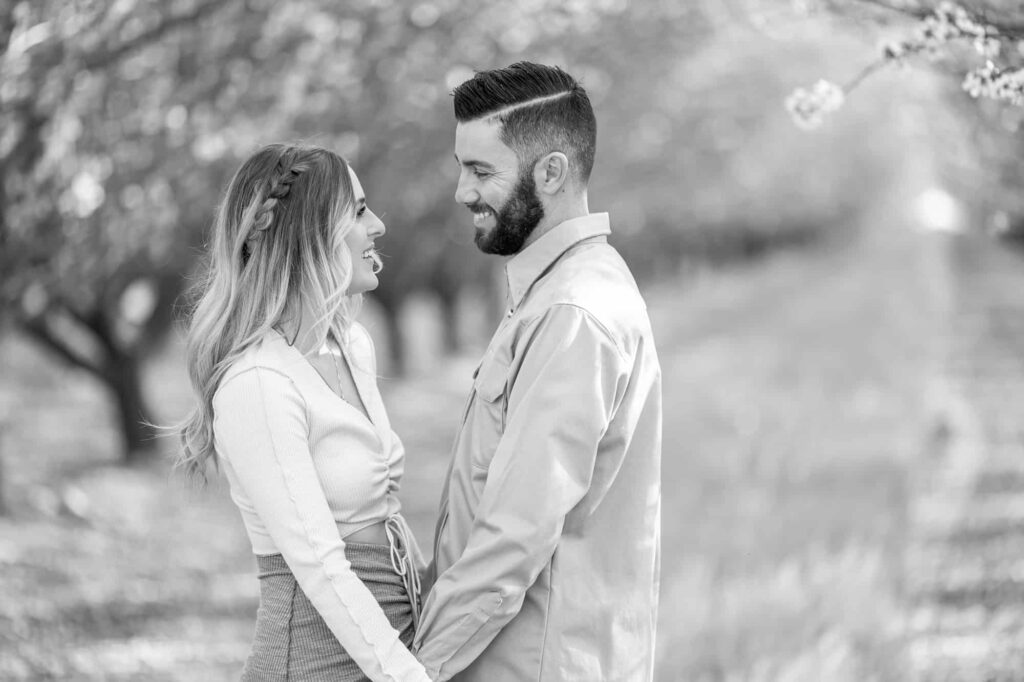 black and white engagement picture of man and woman holding hands and facing each other while smiling in Central Valley almond orchard