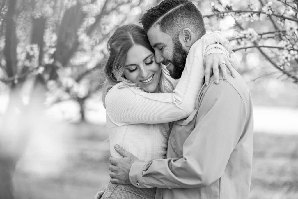 black and white engagement picture with woman holding a man around the neck and they both smile and the man looks down at the woman