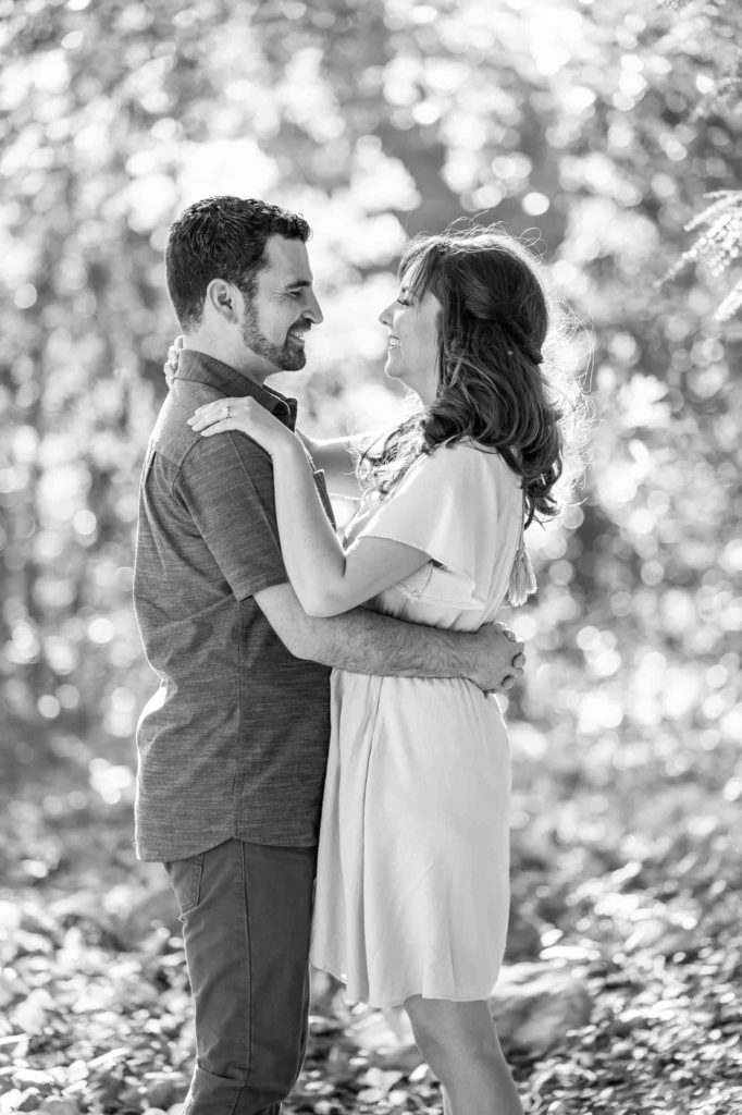 black and white engagement portraits with man and woman facing each other and smiling in the woods