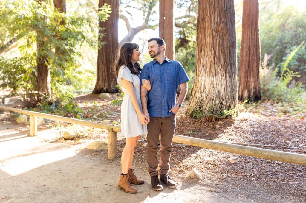 man and woman holding hands while standing on a trail together with redwoods behind them at Santa Barbara Botanical Gardens