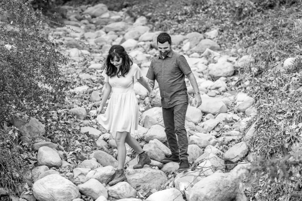 man and woman holding hands as they hike through a rock river bed in Botanical Gardens