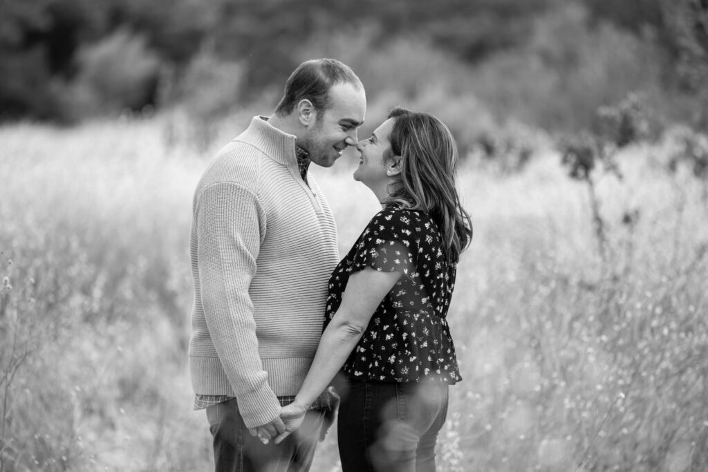 black and white engagement photography in Malibu with man and woman holding hands and leaning into each other so that their noses touch