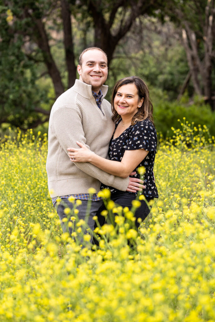 summer engagement session with man and woman embracing in a yellow wildflower field for their outdoor California engagement photos