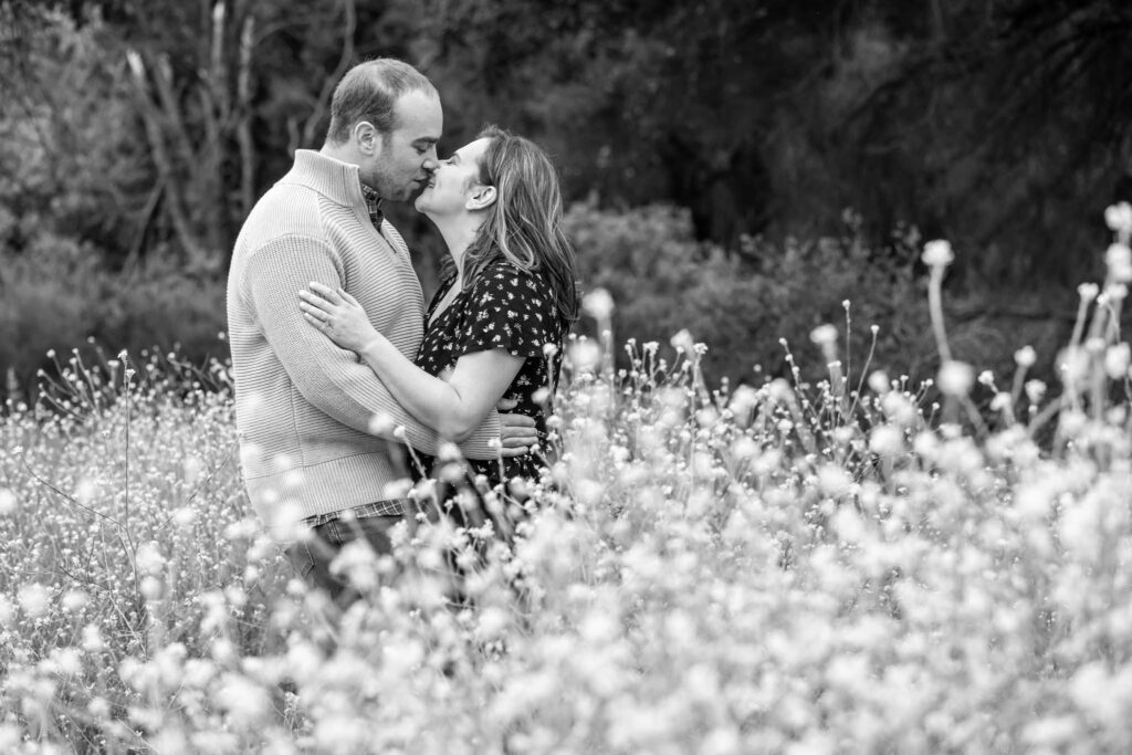 man and woman kissing in a California wild flower field captured by Ventura County engagement photographer