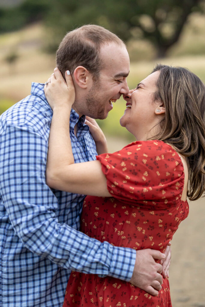 outdoor California engagement photos with man and woman embracing and laughing as they lean into kiss each other