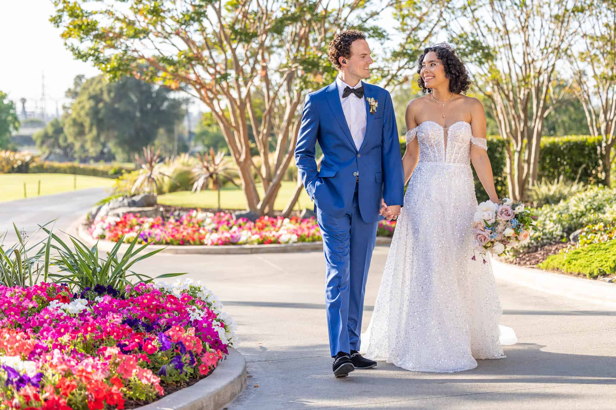 bride and groom hold hands and walk through a garden together for their outdoor bridals
