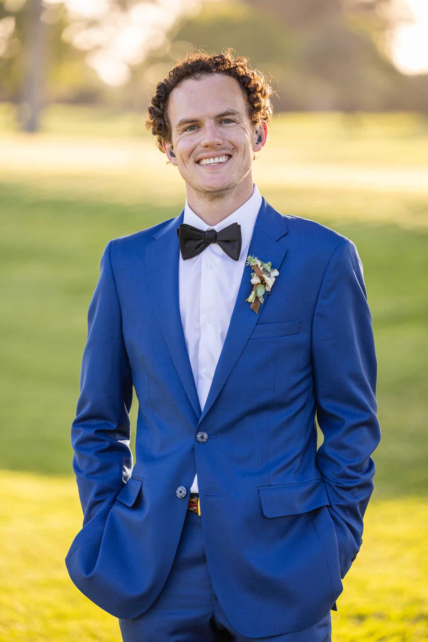 young groom in a blue suit with a black bow tie with his hands in his pockets