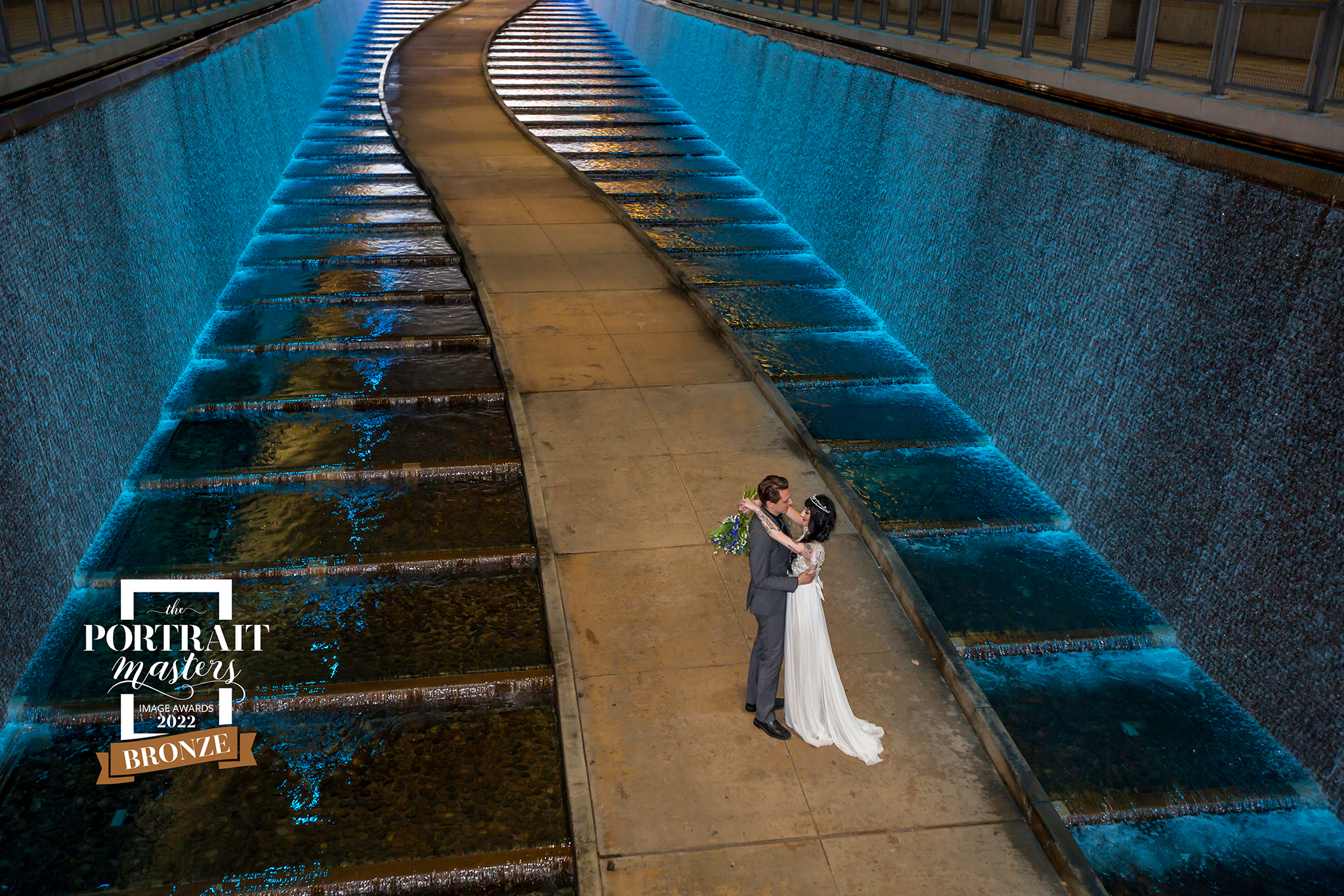 bronze award wedding couple standing in a walkway surrounded by blue water