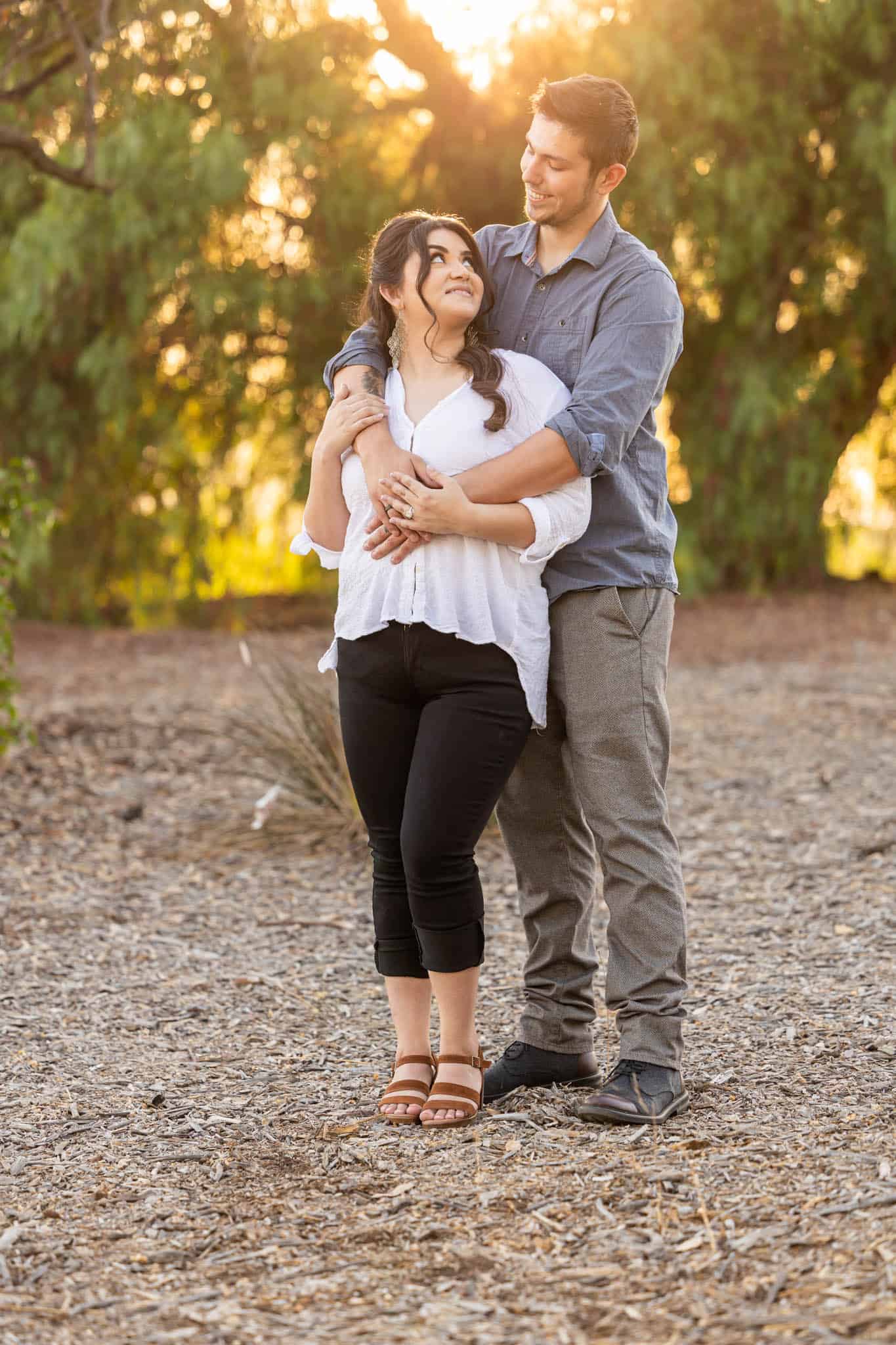Thousand Oaks engagement pictures in Conejo Botanical Gardens with man standing behind woman and holding her around the shoulder as their romantically look at one another