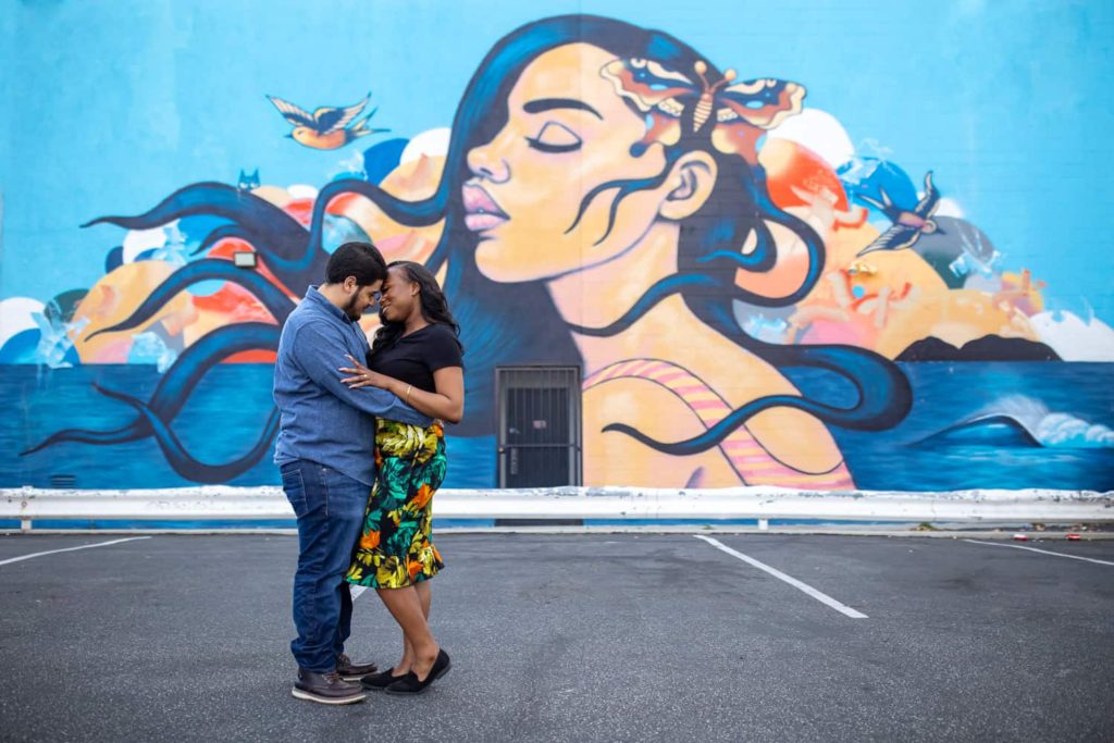 mixed race couple embracing each other in front of a mural of an ethnic woman with flowing hair