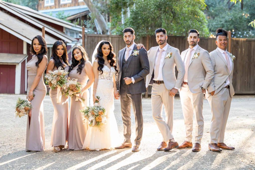 bridal party portrait with bridesmaids, groomsmen, bride and groom posing with the sun shinging behind them at outdoor wedding venue in Malibu